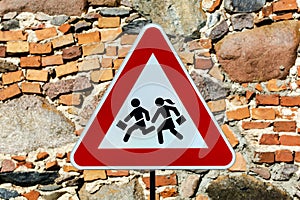 Triangular warning `children crossing` school road traffic sign with stone masonry wall behind