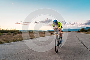 Triathlete riding his bicycle during sunset, preparing for a marathon. The warm colors of the sky provide a beautiful