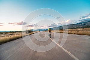 Triathlete riding his bicycle during sunset, preparing for a marathon. The warm colors of the sky provide a beautiful