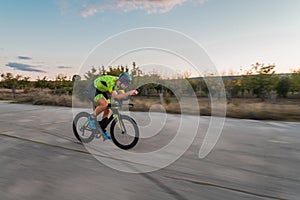 Triathlete riding his bicycle during sunset, preparing for a marathon. The warm colors of the sky provide a beautiful