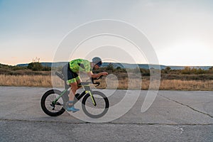 Triathlete riding his bicycle during sunset, preparing for a marathon. The warm colors of the sky provide a beautiful