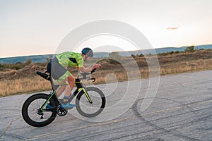 Triathlete riding his bicycle during sunset, preparing for a marathon. The warm colors of the sky provide a beautiful