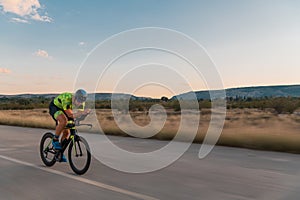 Triathlete riding his bicycle during sunset, preparing for a marathon. The warm colors of the sky provide a beautiful