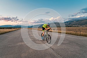 Triathlete riding his bicycle during sunset, preparing for a marathon. The warm colors of the sky provide a beautiful