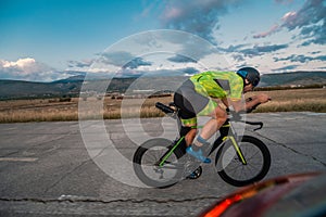 Triathlete riding his bicycle during sunset, preparing for a marathon. The warm colors of the sky provide a beautiful