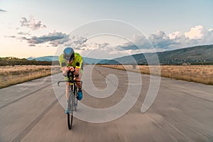 Triathlete riding his bicycle during sunset, preparing for a marathon. The warm colors of the sky provide a beautiful