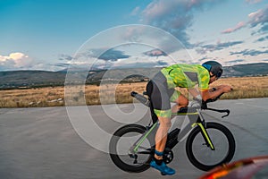 Triathlete riding his bicycle during sunset, preparing for a marathon. The warm colors of the sky provide a beautiful