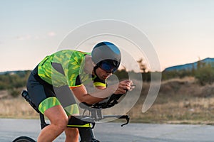 Triathlete riding his bicycle during sunset, preparing for a marathon. The warm colors of the sky provide a beautiful