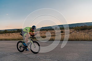 Triathlete riding his bicycle during sunset, preparing for a marathon. The warm colors of the sky provide a beautiful