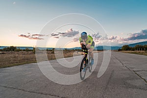 Triathlete riding his bicycle during sunset, preparing for a marathon. The warm colors of the sky provide a beautiful