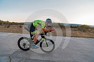 Triathlete riding his bicycle during sunset, preparing for a marathon. The warm colors of the sky provide a beautiful