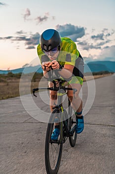 Triathlete riding his bicycle during sunset, preparing for a marathon. The warm colors of the sky provide a beautiful