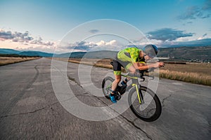 Triathlete riding his bicycle during sunset, preparing for a marathon. The warm colors of the sky provide a beautiful