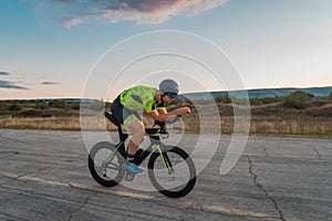 Triathlete riding his bicycle during sunset, preparing for a marathon. The warm colors of the sky provide a beautiful