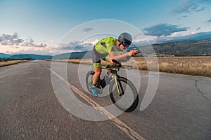 Triathlete riding his bicycle during sunset, preparing for a marathon. The warm colors of the sky provide a beautiful