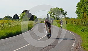 Triathletes on road cycling stage of triathlon fields and trees in background.