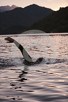 Triathlon athlete swimming on lake in sunrise wearing wetsuit