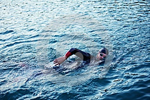 Triathlon athlete swimming on lake in sunrise wearing wetsuit