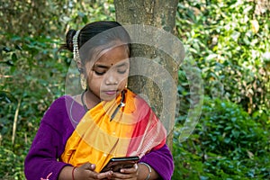 A tribal little girl is listening to music with Bluetooth headphones on her android phone