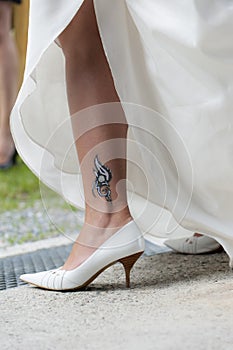 Tribal tatto on leg of a bride with white shoes an