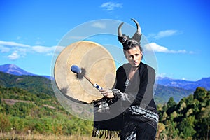 Tribal woman with horns playing a Buffalo drum on the mountain