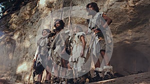 Tribe of Hunter-Gatherers Wearing Animal Skin Holding Stone Tipped Tools, Stand Near Cave Entrance