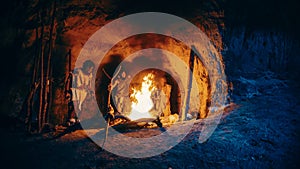 Tribe of Prehistoric Hunter-Gatherers Wearing Animal Skins Stand Around Bonfire Outside of Cave at