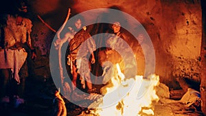 Tribe of Prehistoric Hunter-Gatherers Wearing Animal Skins Stand Around Bonfire Outside of Cave at