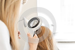 A trichologist examines the condition of the hair on the patient head with a dermatoscope. In a bright cosmetology room