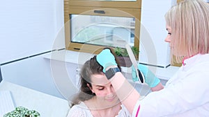 A trichologist examines the condition of the hair on the patient's head using a lens