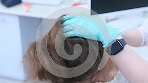 A trichologist examines the condition of the hair on the patient's head using a lens