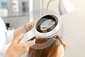 A trichologist examines the condition of the hair on the patients head with a dermatoscope. In a bright cosmetology room