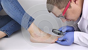 A trichologist examines a toenail with a magnifying glass, which is affected by the fungus. Treatment of mycosis and assistance to