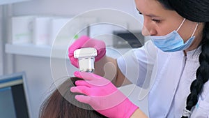 Trichologist examines woman patient hairs using computer trichoscopy in clinic.