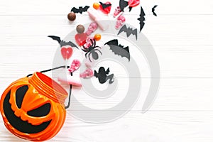 Trick or treat. Halloween candy spilled from jack o lantern bucket with skulls, black bats, ghost, spider decorations on white