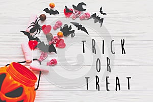 Trick or treat text, happy Halloween sign. Halloween candy spilled from jack o lantern bucket with skulls, black bats, ghost,