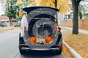 Trick or trunk. Black car trunk decorated for Halloween. Autumn fall decor with red pumpkins and yellow leaves for traditional