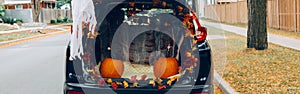 Trick or trunk. Black car trunk decorated for Halloween. Autumn fall decor with red pumpkins and yellow leaves for traditional