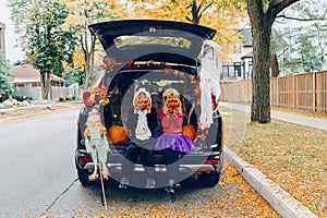 Trick or trunk. Children celebrating Halloween in trunk of car. Boy and girl with red pumpkins celebrating traditional October