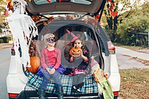 Trick or trunk. Children siblings sisters celebrating Halloween in trunk of car. Friends kids girls preparing for October holiday