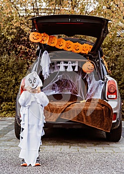 Trick or trunk. Trunk or treat. Little child in ghost costume celebrating Halloween party in decorated trunk of car.