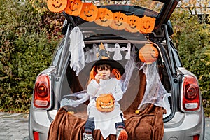 Trick or trunk. Trunk or treat. Little child in witch hat celebrating Halloween party in decorated trunk of car