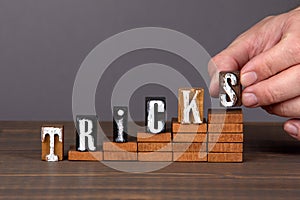 TRICKS concept. Wooden alphabet letters on steps. Gray background