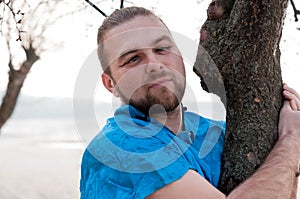 Tricky bearded man in blue kimono with hair sticks hugging tree and roll ones eyes