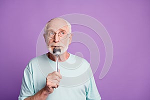 Tricky funny pensioner hold spoon in mouth joking look empty space wear blue t-shirt isolated on violate color
