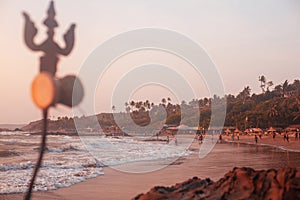 Trident totem near Shiva Face Rock Carving on Vagator Beach, Goa, India. Beautiful sunset and shore background. Northernmost beach