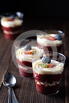 Trifle red velvet. Cake layered dessert in glass decorated with fresh berryes. In a small bowl are strawberry, blueberry, mint