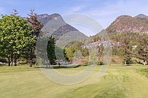Trimmed golf course, tall trees, private houses and cottages on the mountainside, in the woods