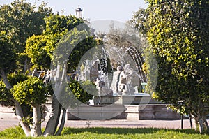 Trimmed trees on the background of a fountain in the Battery Park in Torremolinos, Spain. Parque La Bateria. Bright greenery in th photo