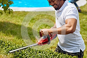 Trimming with Precision: Afro-American Gardener Expertly Tackles Hedges with Hedge Trimmer